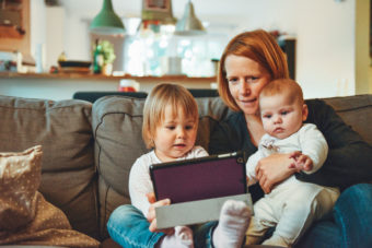 woman with two small children on couch looking at ipad